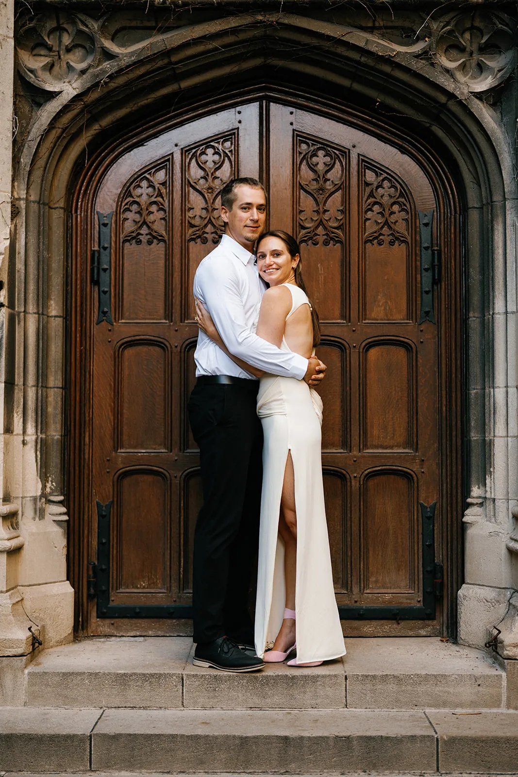 Dany and Cam in front of an arched wooden door