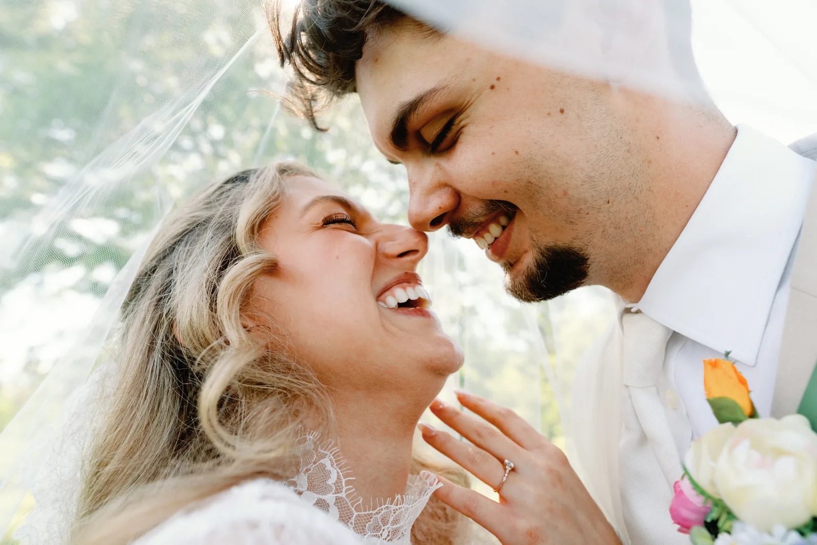 A bride and groom laughing nose to nose under her veil